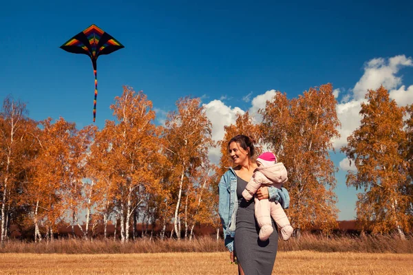 The concept of livestyle and family outdoor recreation in autumn. A young pregnant woman with baby enjoys nature and plays with a kite on a warm autumn sunny day in the background of a field and yellow trees.