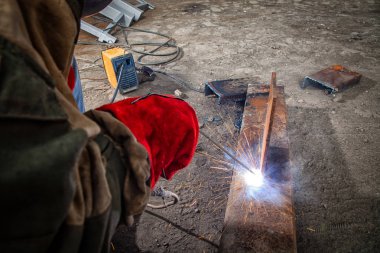 Kahverengi çalışma giysileri kaynaklar bir Oluşturucu kaynakçı bir metal ürün ark kaynak makinesi fabrikası, araçları ve inşaat, parlak ışıklar ve sparks bir sürü ile yakın çekim