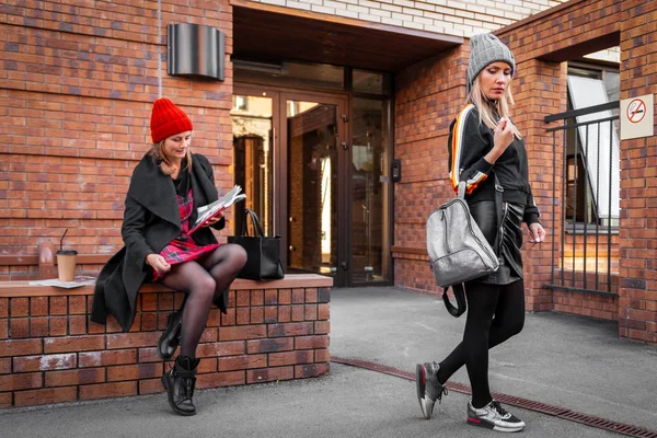 A young women friends in a stylish clothes   walking, chat  and drink coffee to go om old brick city. The concept of livestyle and outdoor recreation in autumn