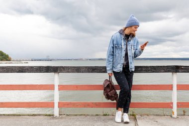 Mavi örgü şapka daimi deniz kenarında güzel bir genç model portresi. Sonbahar sıcak fotoğraf. Kadın gülümsüyor ve göz uzak, neşeli neşeli ruh.