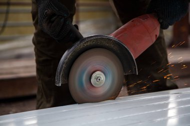 İş giyisi ve siyah eldiven genç bir erkek üreticisi şantiye açı değirmeni ile metal ürün biler