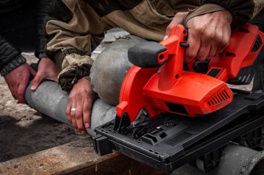 Bir el modern kırmızı daire testere ile inşaat sahasında metal testere bir adam Oluşturucusu'nun yakın çekim. Ağır sanayi işçisi açı değirmeni atölye ile çelik boru kesme. 