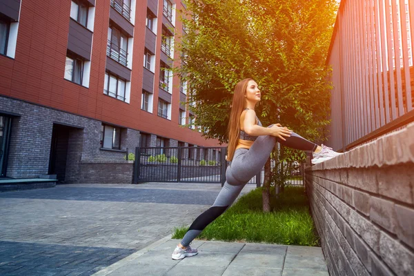 Young woman gymnast with a slim figure in sportswear doing stretching on a city street on a warm summer day. Stretching in the open air