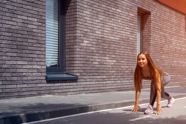 Young woman gymnast with a slim figure in sportswear doing stretching on a city street on a warm summer day. Stretching in the open air