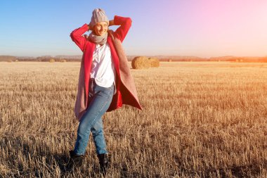 Güzel bir genç model gri örgü şapka ve sıcak giysiler portresi eğlenmene bak, arka plan haystacks güneşli sonbahar gün sahada üzerinde yürüme. Sonbahar sıcak fotoğraf. Gülümseyen kadın ve uzağa bakmak.