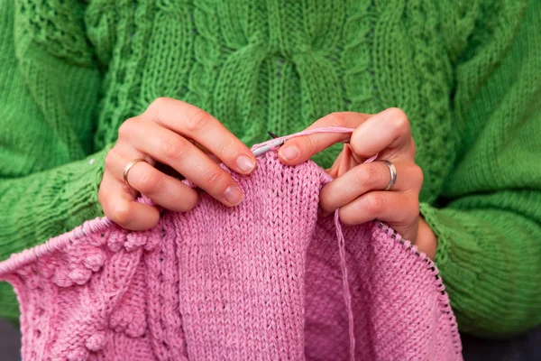 Close-up of a beautiful woman in knitting green sweater knitting needles from a natural woolen thread a pink sweater, a woman shows how to knit correctly