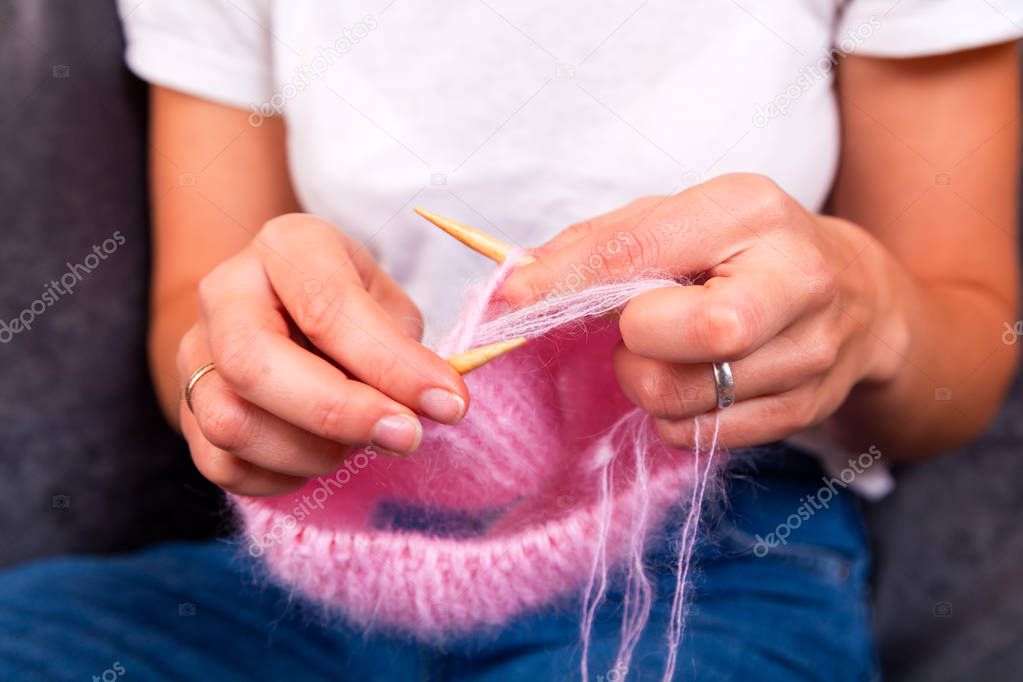 Close-up of an young woman  in white t-shirt and jeans, knits a natural wool hat with knitting needles.
