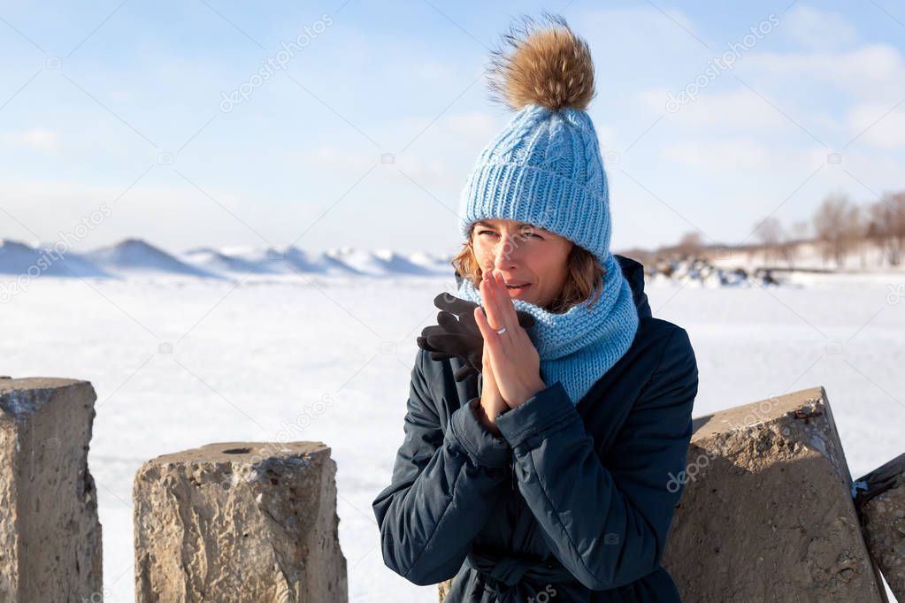 Fashion lifestyle portrait of young trendy woman dressed in warm stylish clothes   warm hands and froze up in the  winter.  portrait of joyful woman, in the background white snow and frozen mountains