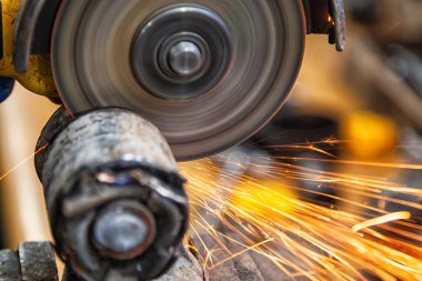 Bir close-up farklı yönlere uçan parlak yanıp söner bir oto tamircisi, araba sessiz bloğunda kesmek için bir metal taşlama kullanarak bir araba tamircisi. Otomatik mekanik çalışmalarını.