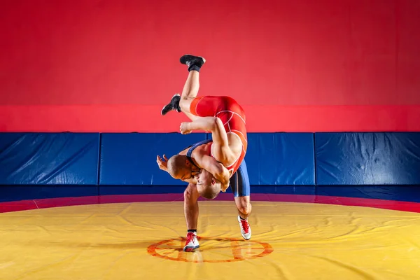 青と赤のタイツをレスリングで つの若い男性は Wrestlng とジムでカーペットをレスリング黄色の腰投げを作るします 公正なレスリングの概念 — ストック写真