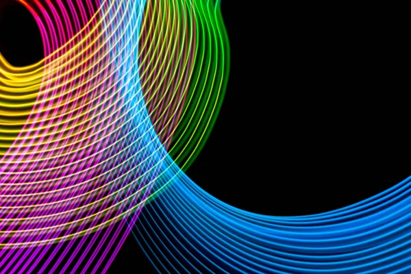 Abstract rainbow neon glowing crossing lines pattern.  Dark background of colorful neon glowing light shapes