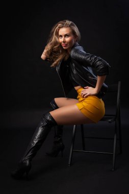 Güzel esmer kız mini etek mutlu gülümseme ile siyah arka plan üzerine poz. Zarif siyah ceketli studio poz kadın modeli gülüyor