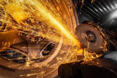 Bir genç adam kaynakçı metal atölyesinde, kıvılcım sinek tarafa bir açı değirmeni taşıyan bir mavi eldiven değirmeni