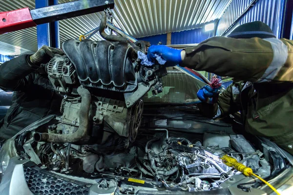 Close-up of the installation of the motor on an old car using a pneumatic manual crane in the auto repair shop. The work of auto mechanics to remove the engine