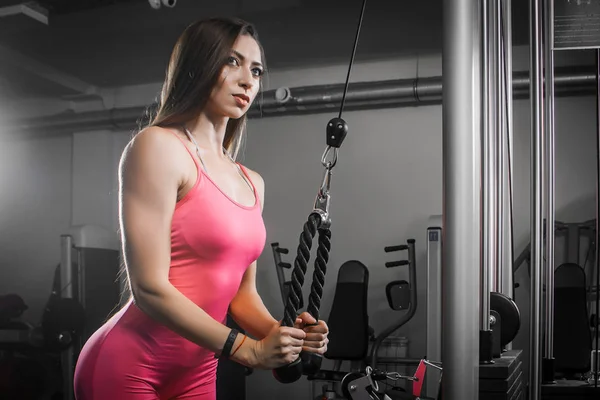Dark-haired woman athlete in a tracksuit shakes hand-triceps biceps on a simulator in the gym. Woman trainer shows how to properly shake hands for women, bending hands on a simulator with a weight