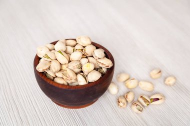 Bir sedir çam plaka ahşap izole arka plan üzerinde soyulmamış fıstık. Kase fıstık fındık ile satır. Soyulmamış Antep fıstığı desen