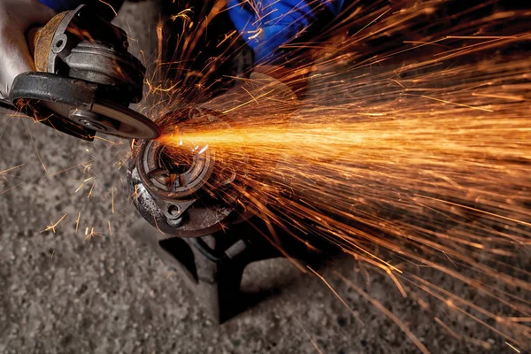 A close-up of a car mechanic using a metal grinder to cut a car part  in an auto repair shop, bright orange flashes flying in different directions, in the background tools for an auto repair