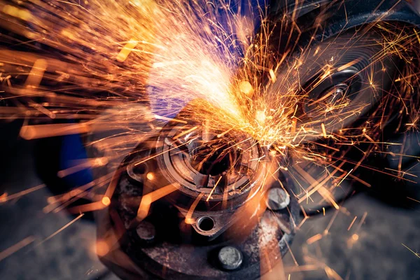 A close-up of a car mechanic using a metal grinder to cut a car part  in an auto repair shop, bright orange flashes flying in different directions, in the background tools for an auto repair