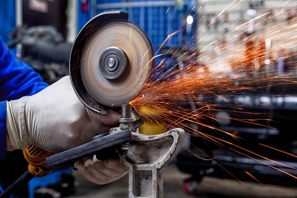 A close-up of a car mechanic using a metal grinder to cut a car silent block in a vise in an auto repair shop, bright flashes flying in different directions, in the background tools for an auto repair shop. Work of auto mechanics.