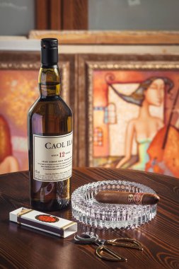 Novosibirsk, Russia - April 07, 2017:  Caol ila Single Malt Whisky,cigar, ashtray and scissors for cigars   at the bar wooden counter  clipart