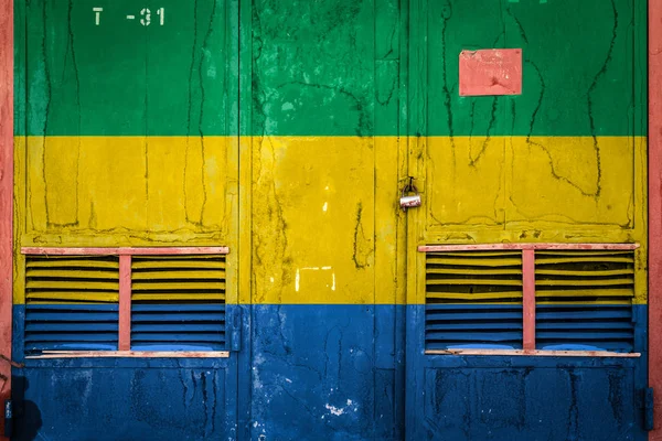 Close-up of old warehouse gate with national flag of Gabon. Concept of Gabon export-import, storage of goods and national delivery of goods. Flag in grunge style