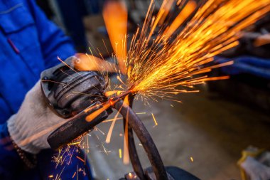 Otomobil tamirhanesinde taşınan bir arabayı kesmek için metal öğütücü kullanan bir araba tamircisinin yakın çekimi, farklı yönlerde uçan parlak ışıklar, bir otomobil tamircisinin arka plan araçları.