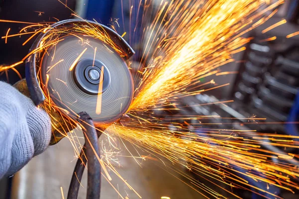 A close-up of a car mechanic using a metal grinder to cut a car bearing  in an auto repair shop, bright flashes flying in different directions, in the background tools for an auto repair