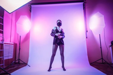 Sahne arkasında: kadın ile siyah iç çamaşırı, külotlu çorap modeli, renkli parlak neon mavi ve pembe Işık Studio cazip konumda poz ceket. Moda kavramı