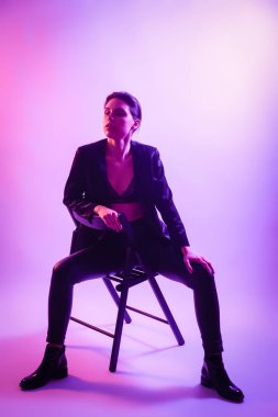 Savaşçı kadını pembe mavi neon ışık, Trendy moda saç modeli. Yüksek moda. Kadın ceket, pantolon ve iç çamaşırı neon ışıkları sandalyede poz sinema gece portresi