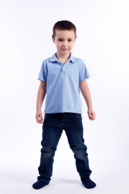 Mavi Jeans, koyu saçlı küçük boy gülümseyerek mavi polo t-shirt poz, gülerek mutlu bir şekilde beyaz bir arka planda bir fotoğraf stüdyosu izole. Mutlu neşeli güzel çocuk portresi
