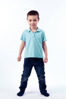 Mavi Jeans, koyu saçlı küçük boy gülümseyerek mavi polo t-shirt poz, gülerek mutlu bir şekilde beyaz bir arka planda bir fotoğraf stüdyosu izole. Mutlu neşeli güzel çocuk portresi