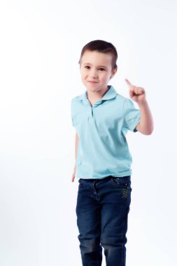 Küçük boy gülümseyerek mavi kot pantolon koyu saçlı, mavi polo t-shirt yemin ediyor ve beyaz izole arka planda bir fotoğraf stüdyosu parmağını gösterir