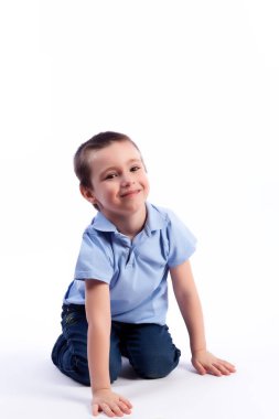 Mavi Jeans, koyu saçlı küçük boy gülümseyerek mavi polo t-shirt katta oturan mutlu bir beyaz izole arka planda bir fotoğraf Studio gülüyor. Mutlu neşeli güzel çocuk portresi