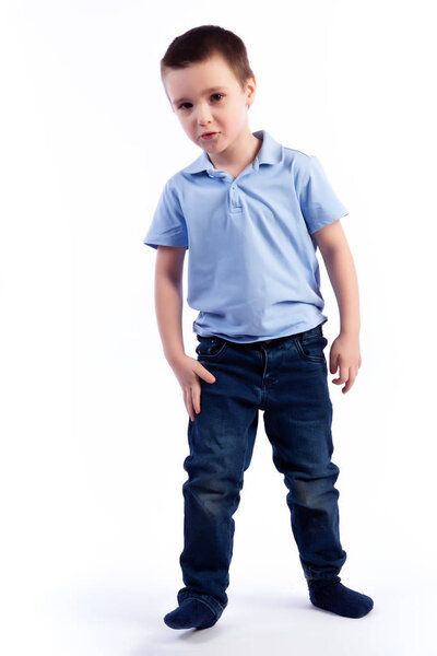 Little smiling boy with dark hair in blue jeans, blue polo t-shirt posing, laughing happily on a white isolated background in a photo studio. Portrait of happy joyful beautiful boy