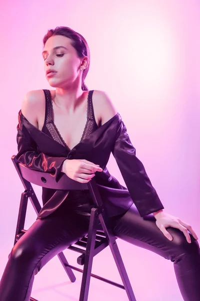 Cinematic night portrait of woman in  neon. High Fashion model girl in colorful bright neon lights posing on chair in studio, portrait of beautiful woman in   jacket, underwear and trousers.