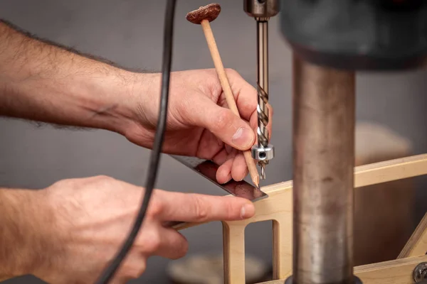 Close up of experienced carpenter in work clothes and small buiness owner measures a wooden board with a marks with pencil the necessary points for slices