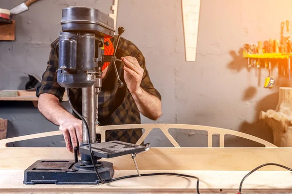 Close up of a man with work clothes and a carpenter\'s cap is carving a wooden board on an modern large drilling machine in a light workshop. Home repair concepts