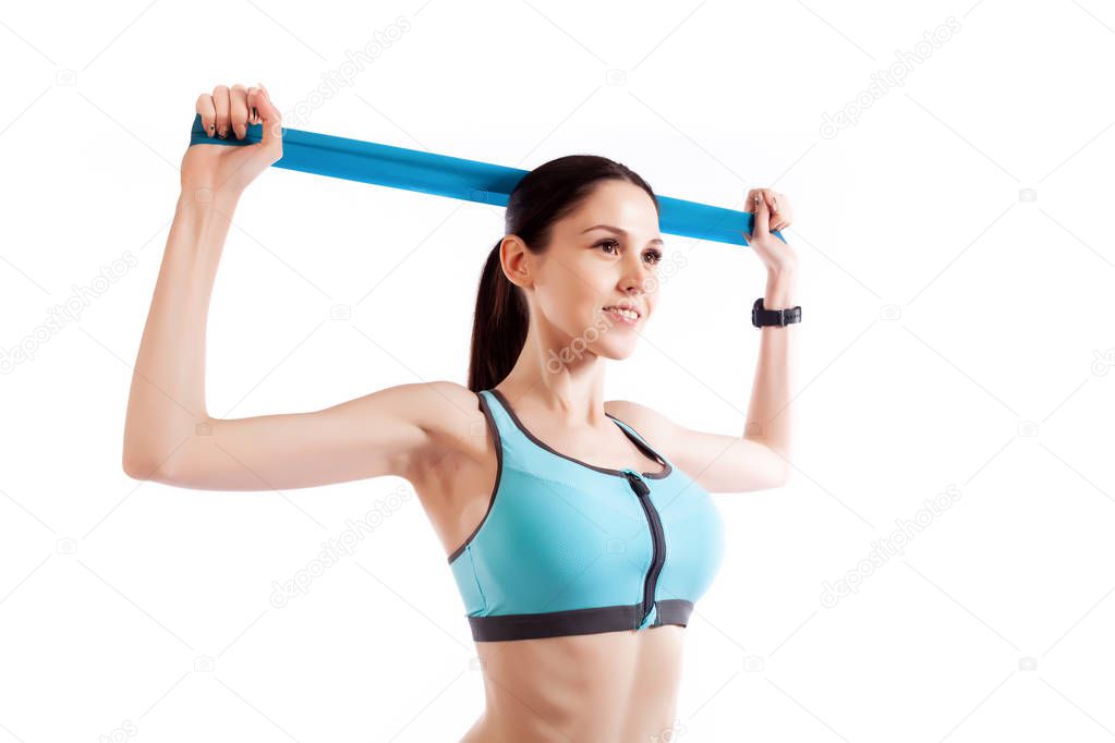 A dark-haired woman coach in a sporty short top and gym leggings exercise for your back, hands behind his head breeding with sport fitness rubber bands on a  white isolated background in studio 