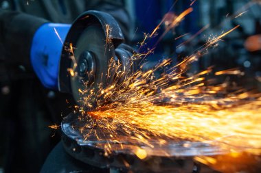 Bir oto tamir atölyesinde fren diskini kesmek için metal öğütücü kullanan bir araba tamircisinin yakın çekim, farklı yönlerde uçan parlak yanıp söner, bir oto tamir imal arka plan araçlarında