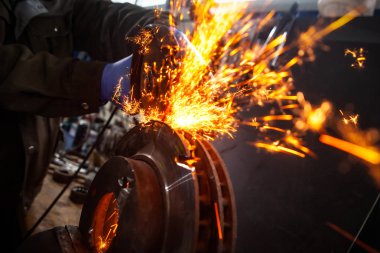 Bir el dairesel testere ile metal fren diski taşıyan bir adam testere yakın çekim, parlak yanıp söner farklı yönlere uçan, bir oto tamir dükkanı için arka plan araçları. Oto mekanik çalışmaları.