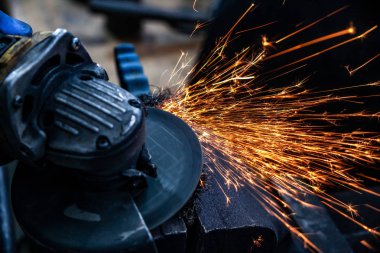 Bir el dairesel testere ile metal fren diski taşıyan bir adam testere yakın çekim, parlak yanıp söner farklı yönlere uçan, bir oto tamir dükkanı için arka plan araçları. Oto mekanik çalışmaları.
