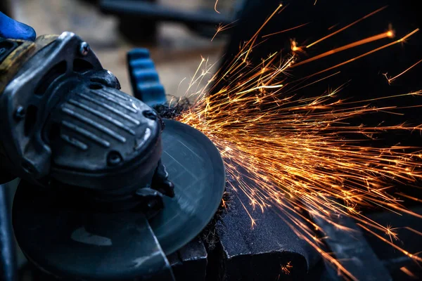 Bir el dairesel testere ile metal fren diski taşıyan bir adam testere yakın çekim, parlak yanıp söner farklı yönlere uçan, bir oto tamir dükkanı için arka plan araçları. Oto mekanik çalışmaları.