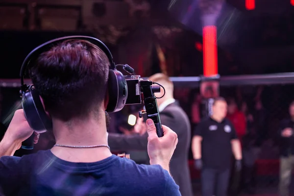 Video filming in the backstage of a sporting event. Athletes fighters in oktogon in front of the camera after the fight. Operator with a professional video camera during the event, rear view