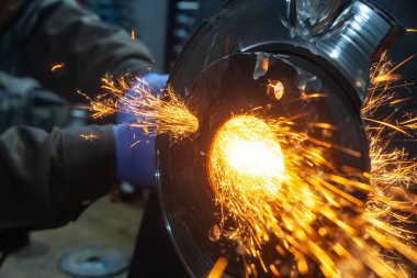 Bir genç adam kaynakçı metal atölyesinde, kıvılcım sinek tarafa bir açı değirmeni taşıyan bir mavi eldiven değirmeni