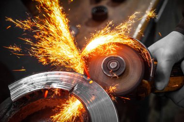 Bir genç adam kaynakçı metal atölyesinde, kıvılcım sinek tarafa bir açı değirmeni taşıyan bir mavi eldiven değirmeni