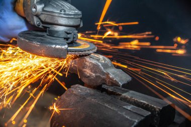 Bir el dairesel testere ile metal çekiç taşıyan bir adam testere yakın çekim, parlak yanıp söner farklı yönlere uçan, bir oto tamir dükkanı için arka plan araçları. Oto mekanik çalışmaları.