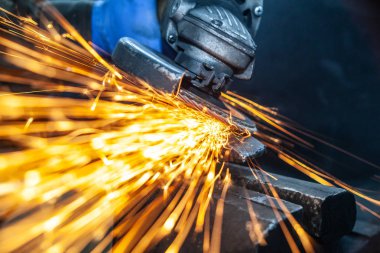 Bir el dairesel testere ile metal çekiç taşıyan bir adam testere yakın çekim, parlak yanıp söner farklı yönlere uçan, bir oto tamir dükkanı için arka plan araçları. Oto mekanik çalışmaları.