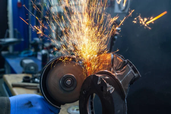 A close-up of a car mechanic using a metal grinder to cut   bearing in an auto repair shop, bright flashes flying in different directions. Work of auto mechanics.