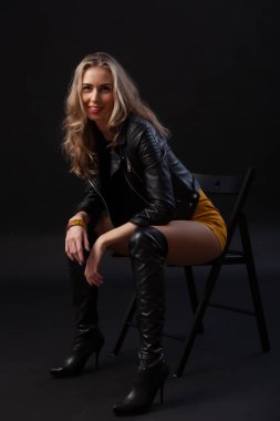 Siyah deri ceket, siyah üst, kısa etek ve siyah arka plan üzerinde çizme giyen sağlıklı vücut ile güzel kadın