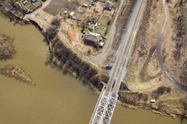 Sıcak güneşli bir günde arka plan ormanı, köy şantiyesinde, demiryolu köprüsü ile nehrin dikey havadan geniş açılı drone görünümü